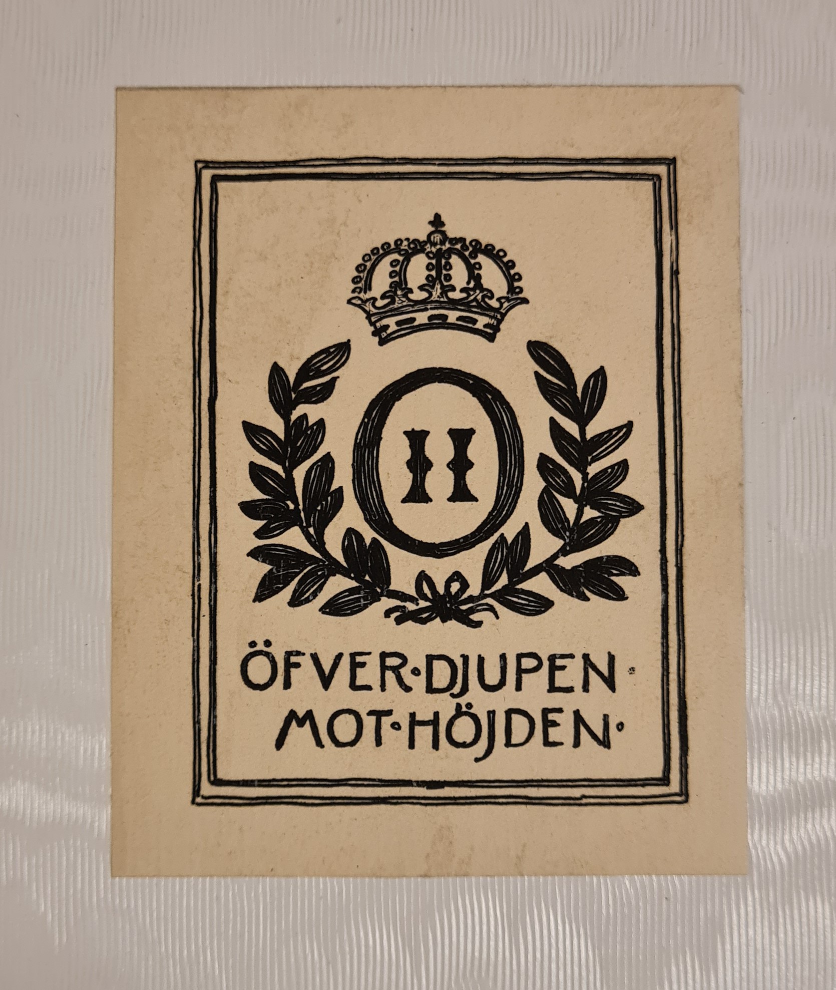 Färgfotografi av ett inramat tryckt monogram med en kungakrona och texten O II, Öfver djupen mot höjden