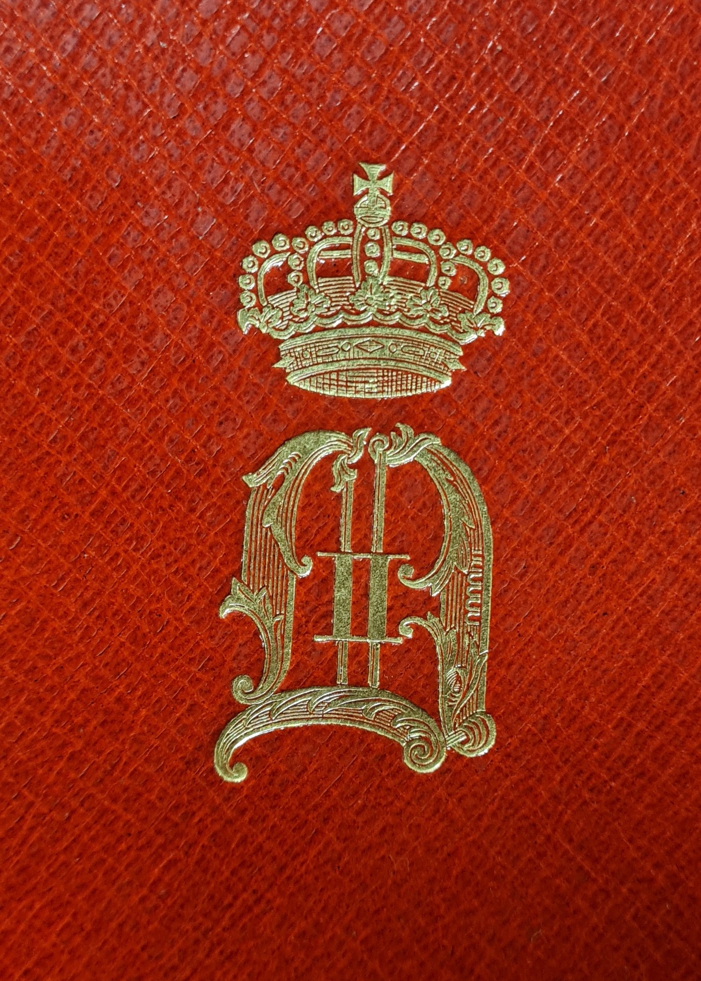 Färgfoto av ett förgyllt monogram med kungakrona på ett rött bokband