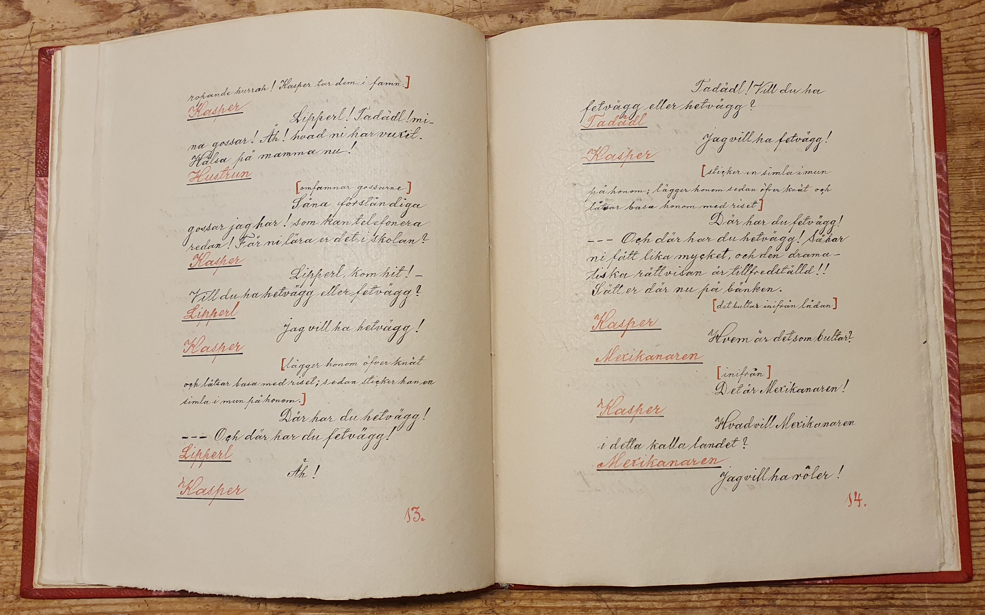 Uppslag med två handskrivna sidor i ett pjäsmanus, texten är skriven med svart och rött på vitt papper. 
