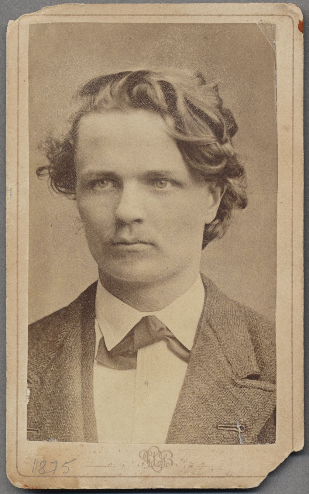 Svartvitt fotografi av ansikte på yngre man med kort, vågigt hår och allvarlig blick.