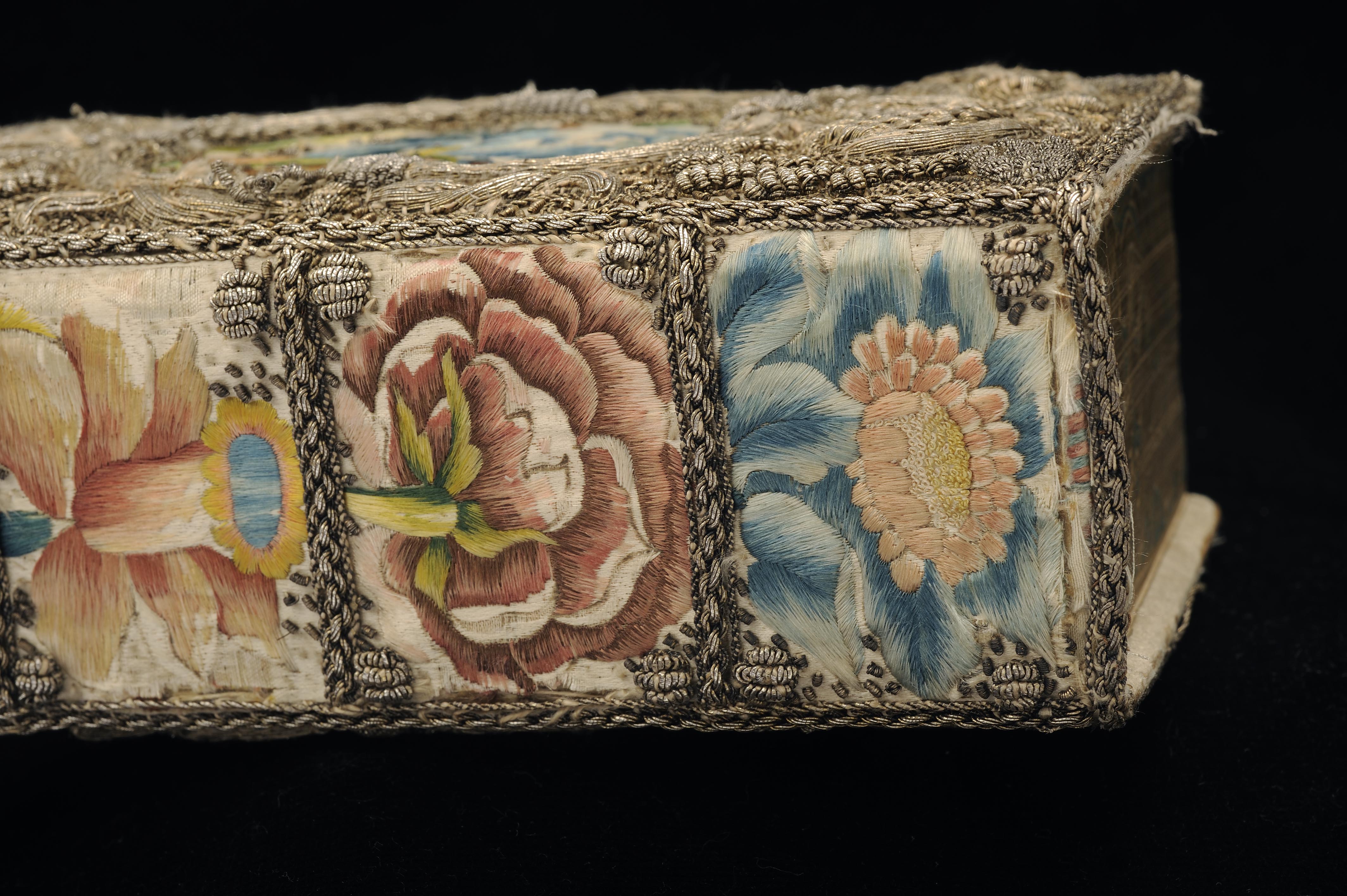 Foto av broderat bokband, detalj av rygg, med blommor broderade i olika färger
