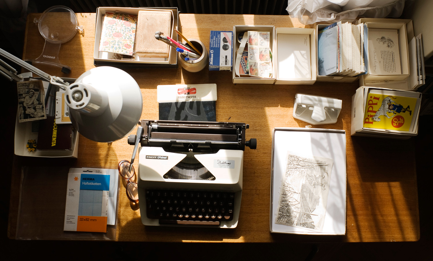 Ett bord med skrivmaskin, papper, vykort och kontorsmaterial.