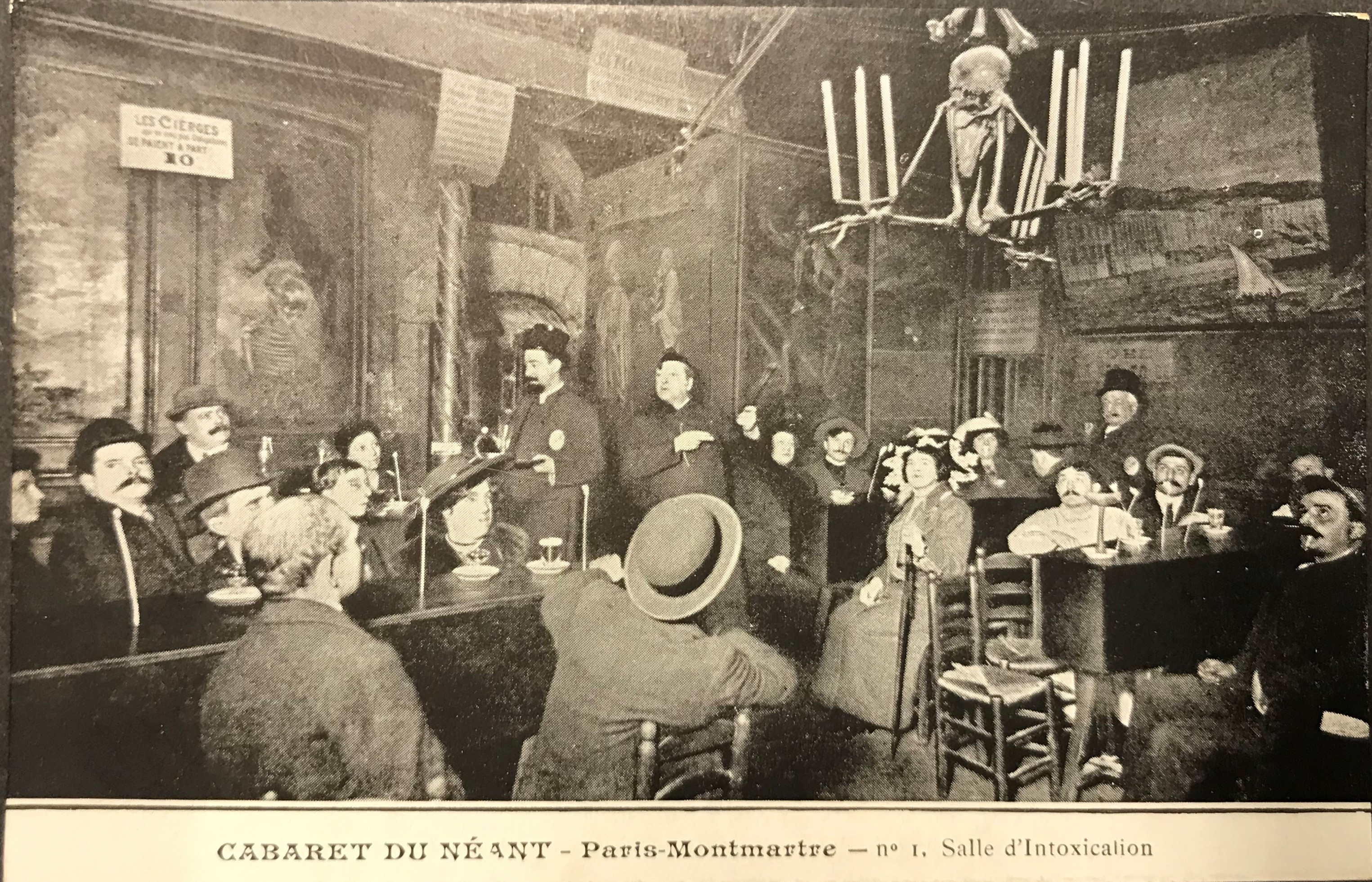 Svartvitt vykort föreställande en sal där människor sitter vid långa bord omgivna av skelett.