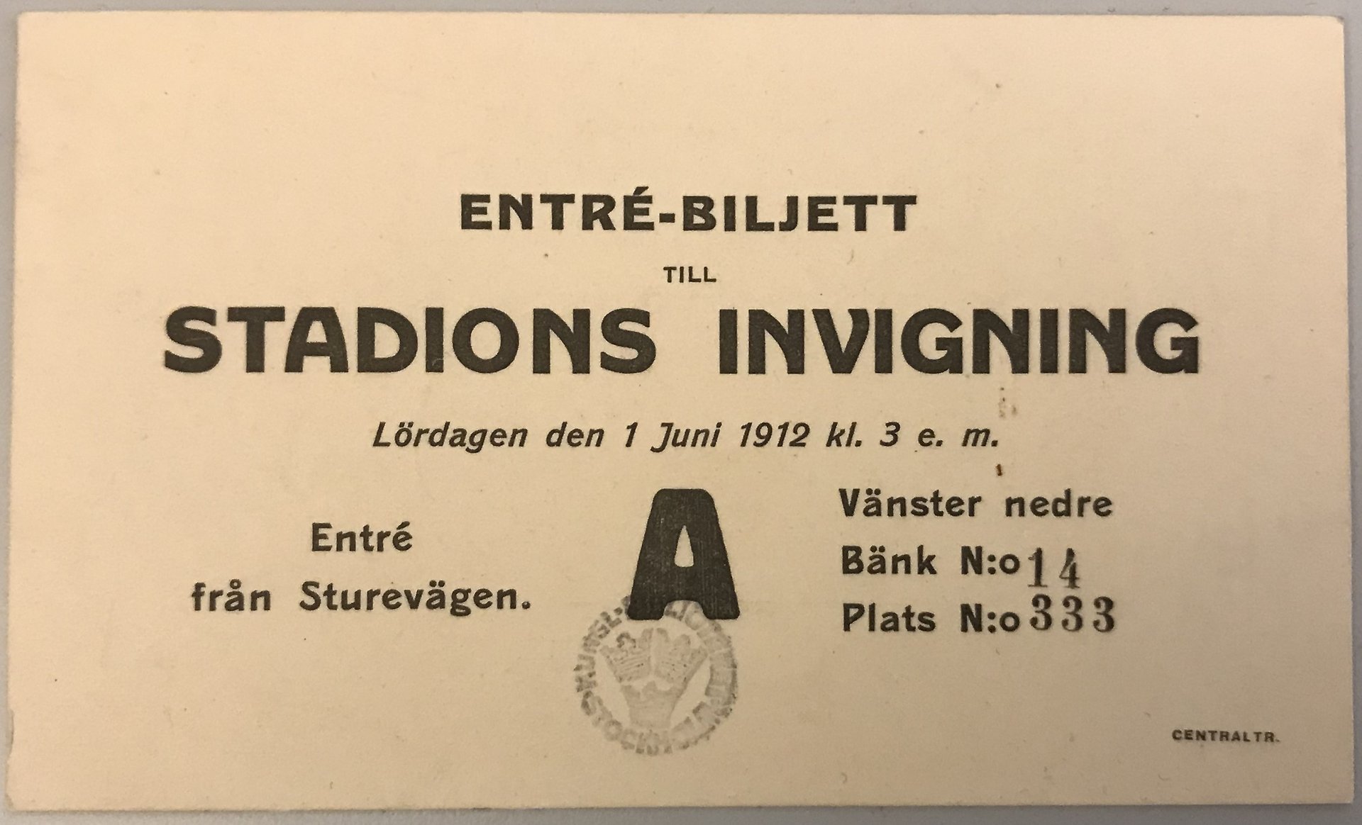 Vit pappersbiljett med tryckt svart text som anger bänk- och platsnummer på Stockholms stadions invigning den 1 juni 1912.