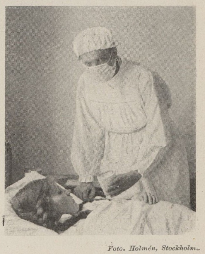 Fotografi på läkare med munskydd som står vid en sjuk flickas säng. 