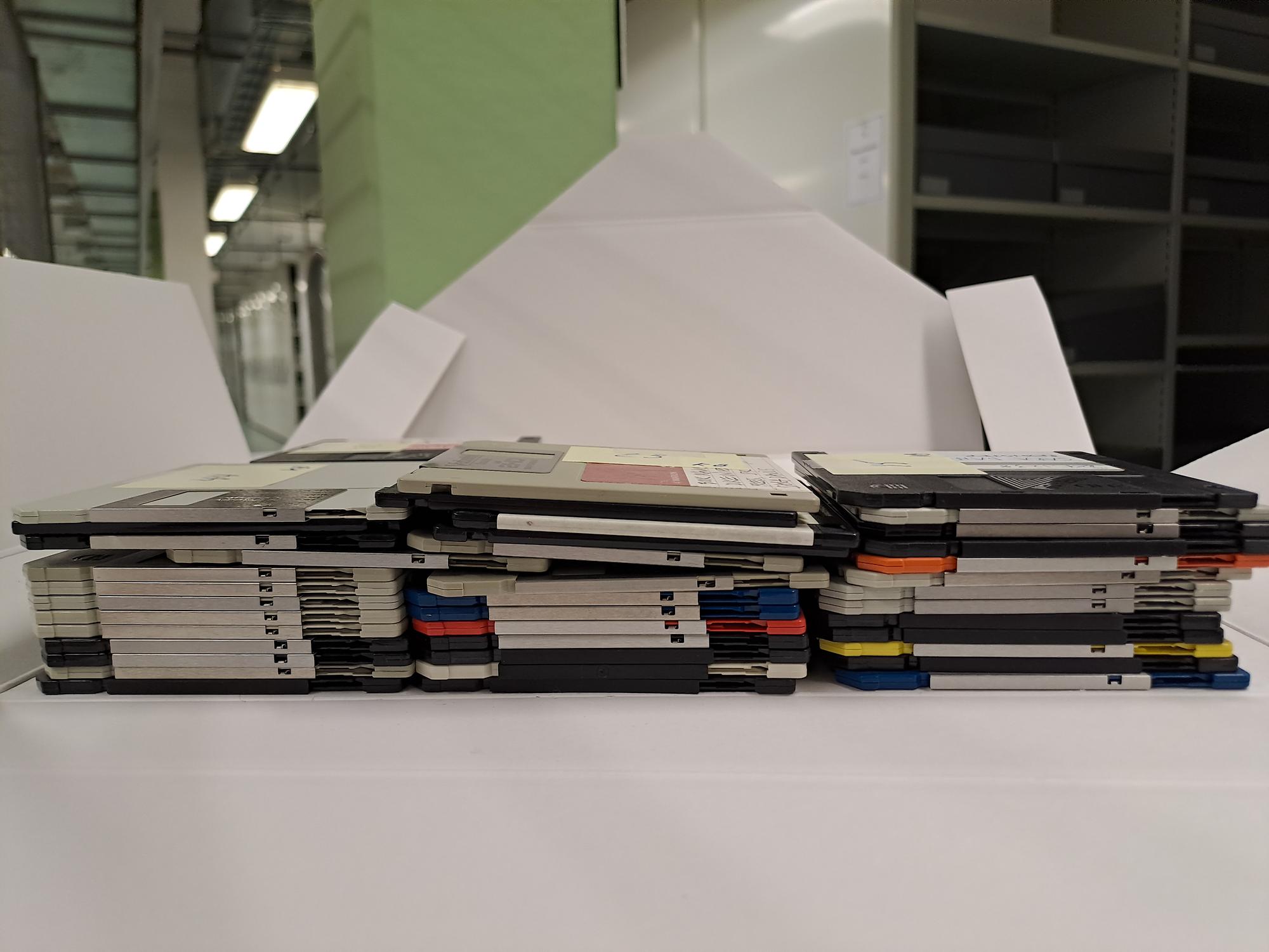Färgfotografi av tre små travar med gamla disketter som ligger i en uppvikt arkivkapsel.