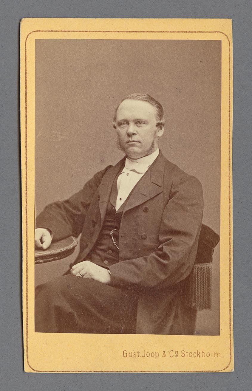 Porträtt av Johan Erik Fröberg sittande i en stol iklädd rock, väst och kravatt.
