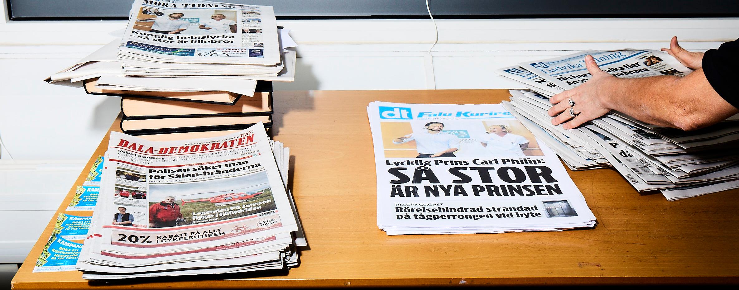 En person rättar till en tidningshög på ett bord med flera tidningshögar.
