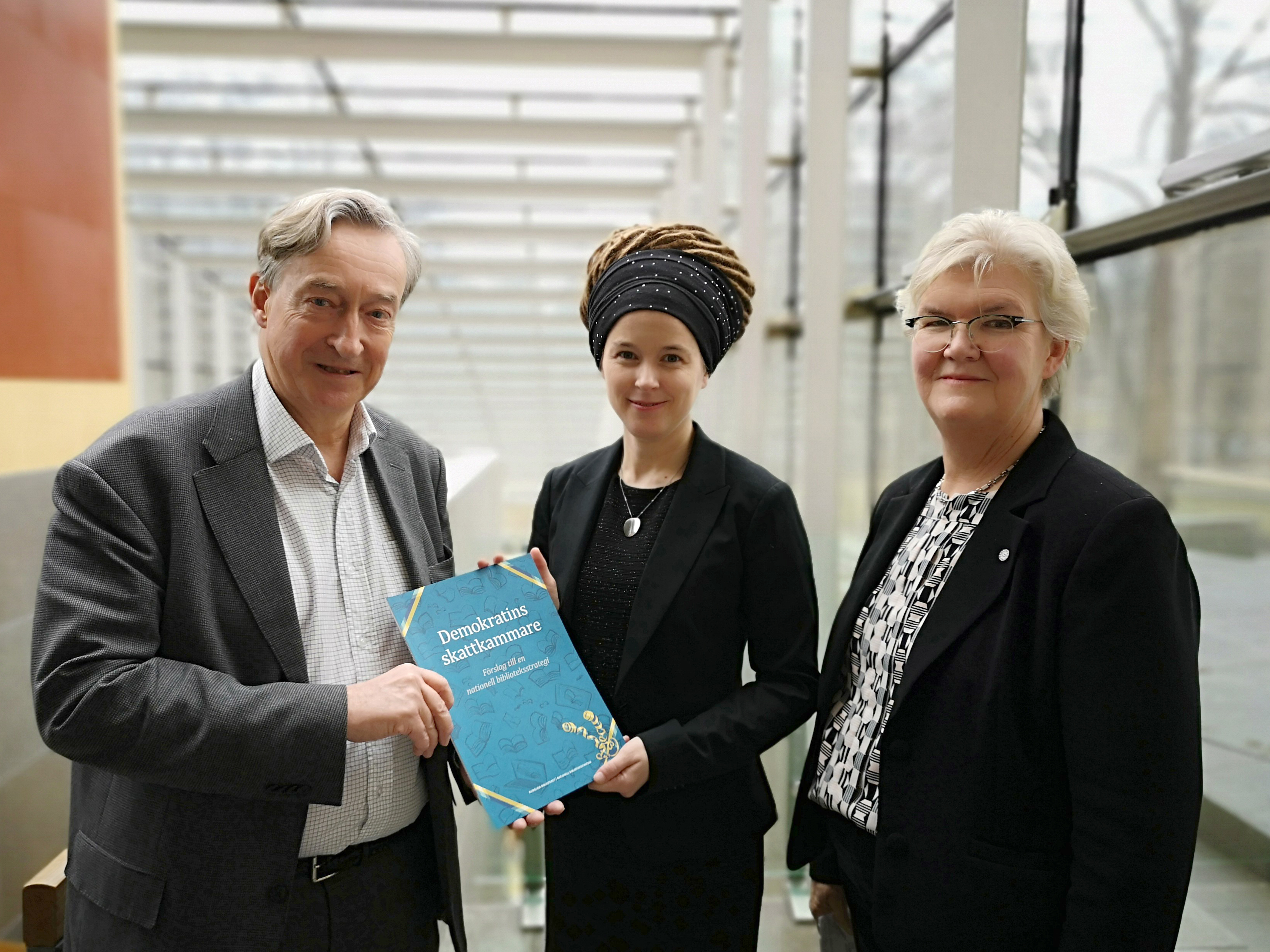 En man och en kvinna håller i en rapport. Bredvid dem står ännu en kvinna.