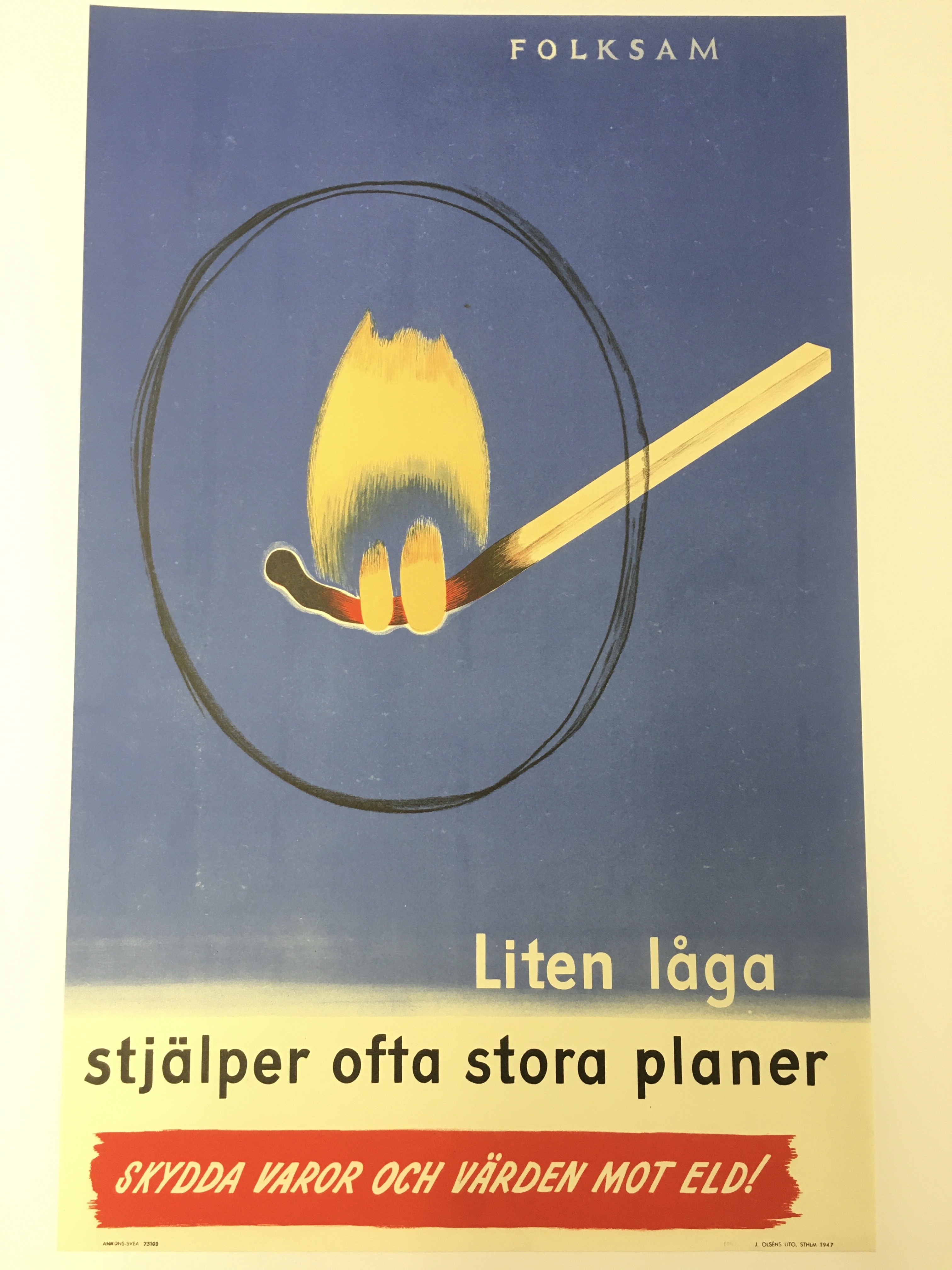 Tecknad affisch med en stor böjd tändstick där elden är markerad med en cirkel. Texten lyder: Liten låga stjälper ofta stora planer. Skydda varor och värden mot eld! Folksam.