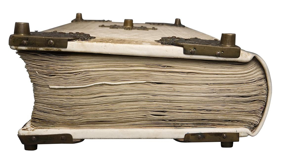 Old book with white cover adorned with metal fittings seen from the side.