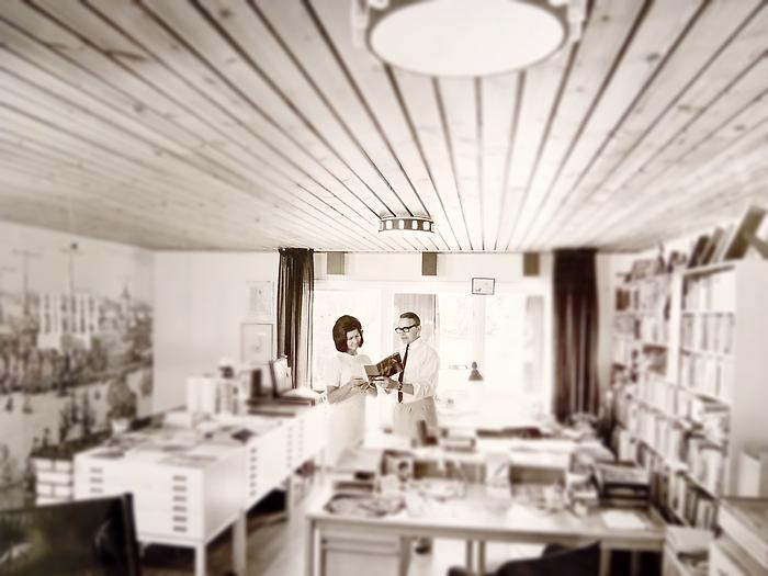 Svartvitt fotografi föreställande en man och en kvinna i ateljé med bokhyllor och skrivbord 