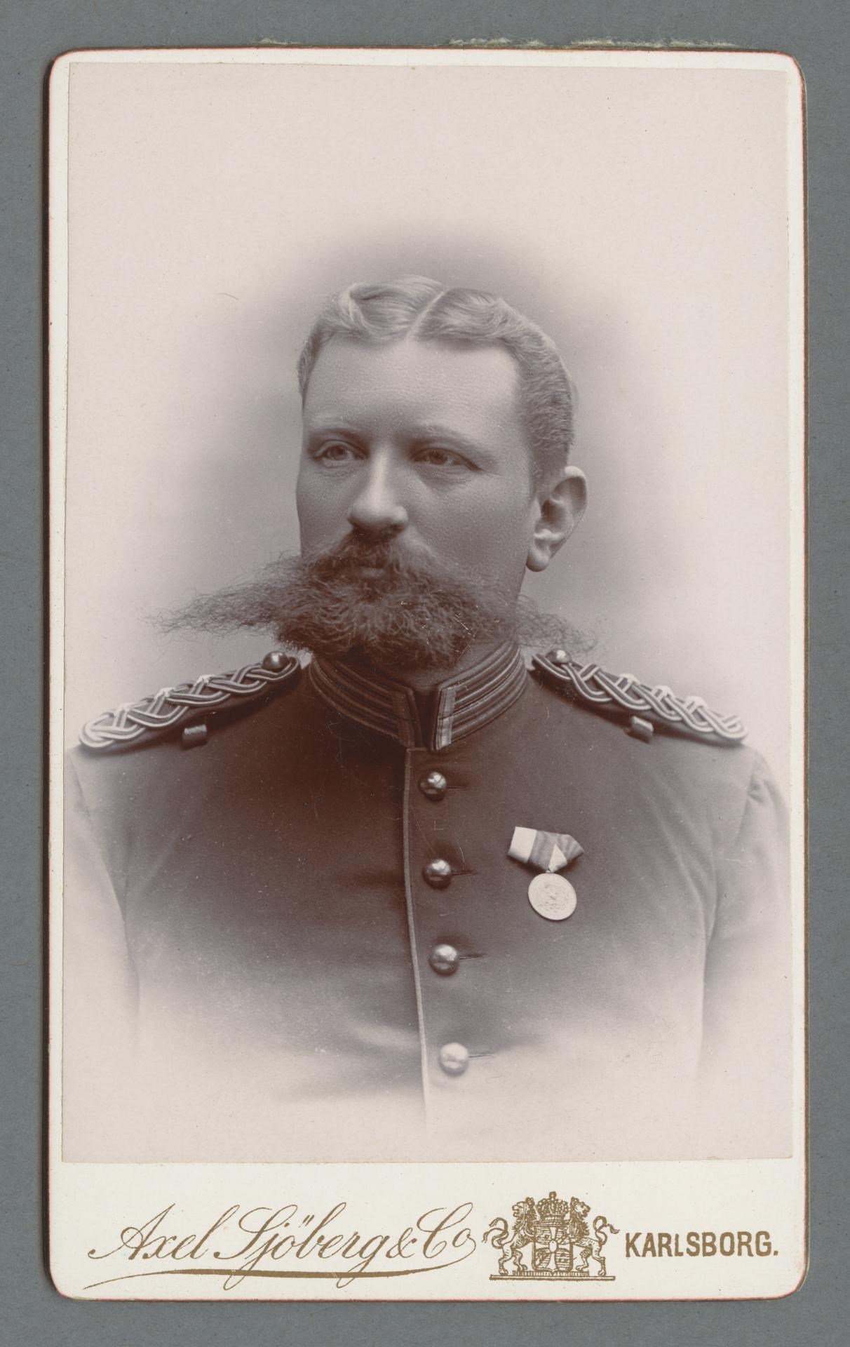Bystporträtt av Gustaf Fleetwood iklädd uniform med distinkt kammad mittbena och stort skägg med mustasch.