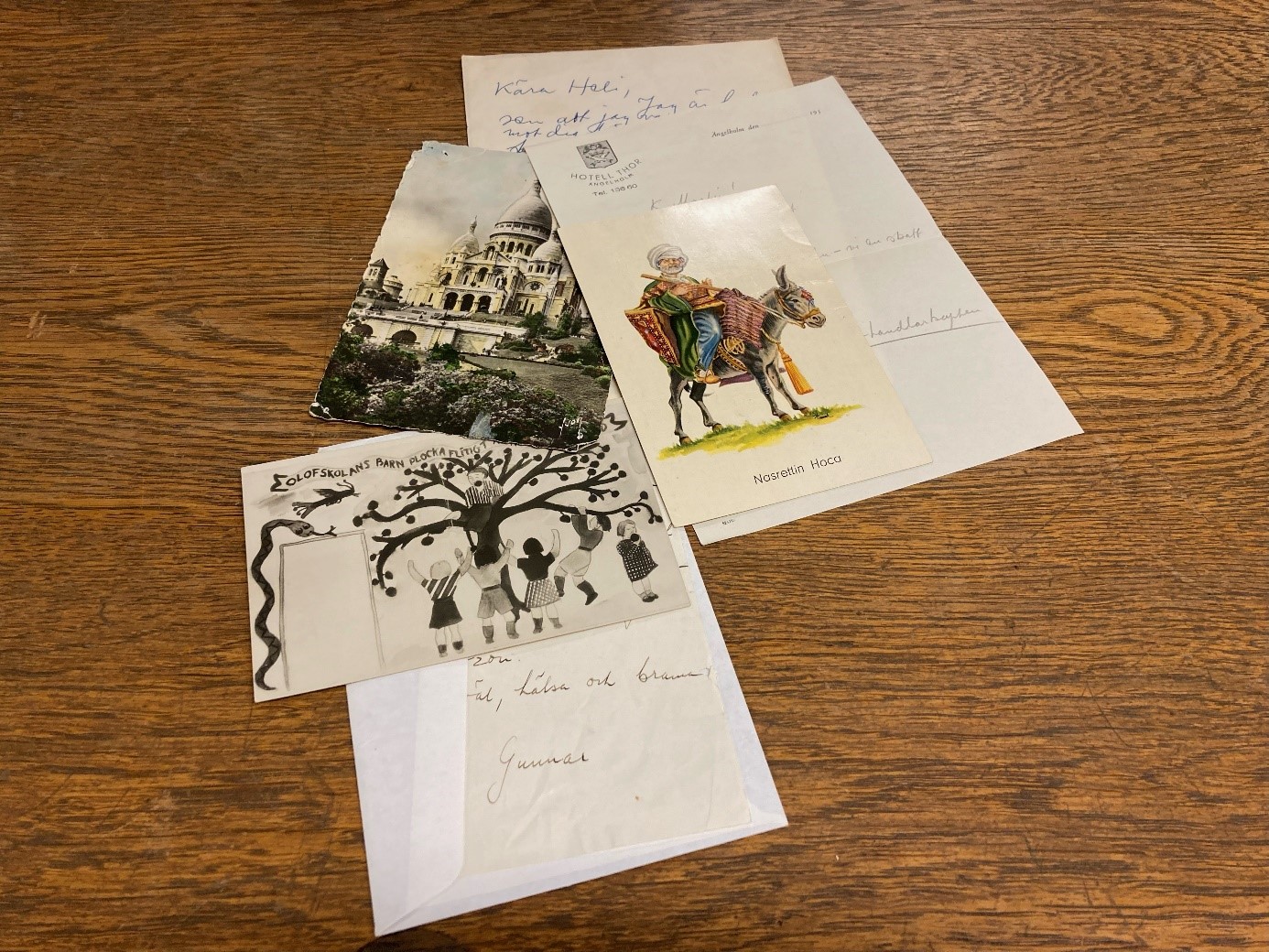 Färgfotografi av tre handskrivna brev och tre vykort med olika motiv som ligger utspridda på en träskiva.