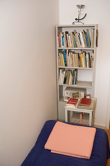 En säng och en smal bokhylla med böcker.