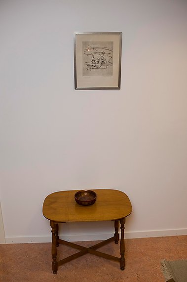 En tavla hänger ovanför ett litet bord. Tavlan visar en abstrakt bild av några streck.