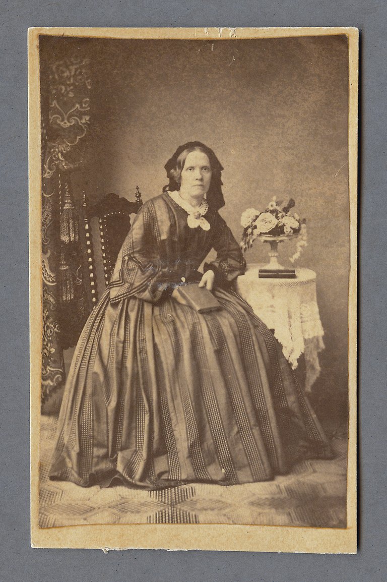 Svartvit fotografi av en kvinna i pampig klänning som sitter ner med en bok i knät.