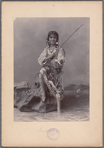 Svartvitt fotografi av en flicka som sitter på en sten och fiskar. Det syns att fotot är taget i en studio och inte utomhus.