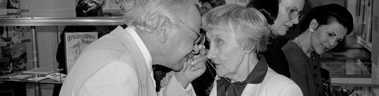 Man och kvinna står panna mot panna, mannen tittar på kvinann genom monokel.