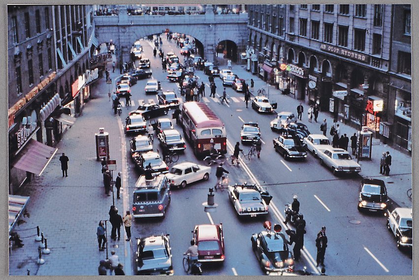 Ett färgfotografi med vy över Kungsgatan där bilar och bussar som stannat nu börjat byta sida av trafiken. Poliser i bilar och till fots samt gångtrafikanter tittar på.