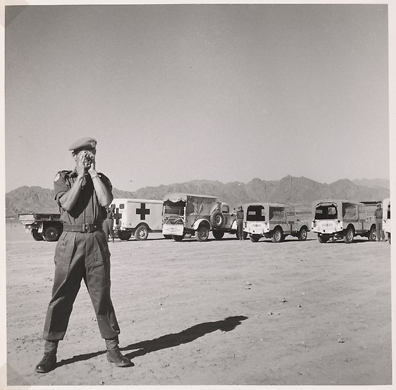 En FN-soldat med kamera, framför parkerade bussar